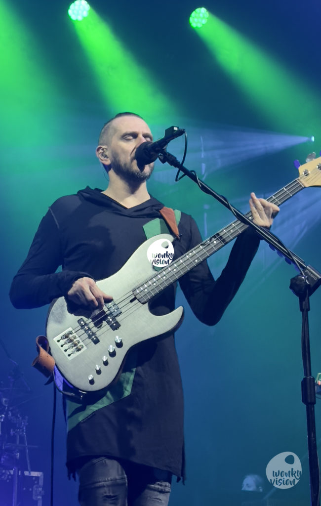 Mariusz from Riverside sings into the microphone while he plays the bass. His eyes are closed. He is lost in the music